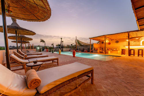 Terrasse sur le toit du Riad Arkaya au crépuscule avec chaises longues, piscine et salon couvert à Essaouira