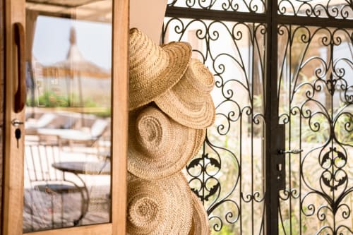 Chapeaux de paille exposés sur les rampes en fer forgé du Riad Arkaya à Essaouira, avec vue sur la terrasse