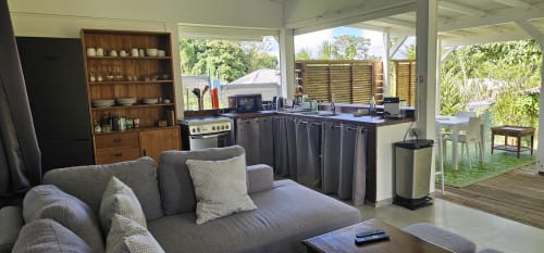 Séjour ouvert avec canapé gris, cuisine, étagères en bois et vue sur la piscine au bungalow Habitation Villa Les Cassias