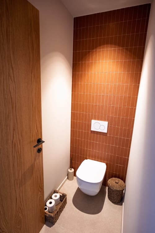 Salle de bain moderne de la villa Can Jeannette avec mur en carrelage rouge, toilettes blanches et paniers de rangement tressés à Collioure