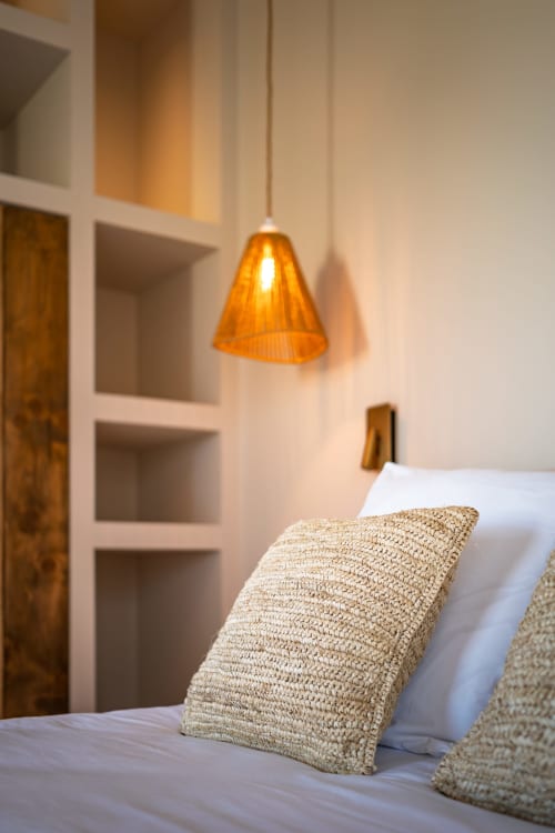 Chambre douillette de la villa Can Jeannette à Collioure avec coussins tissés, luminaire suspendu orange et étagères intégrées