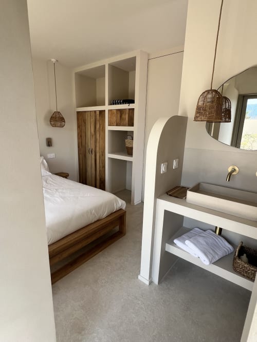 Chambre moderne avec lit en bois, literie blanche, salle de bain attenante avec lavabo, luminaires en rotin tressé et rangements intégrés