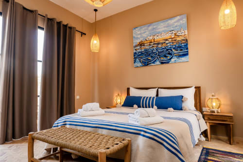 Chambre Mogador au Riad Arkaya à Essaouira avec literie rayée bleue, banc tissé, décoration nautique et ambiance chaleureuse