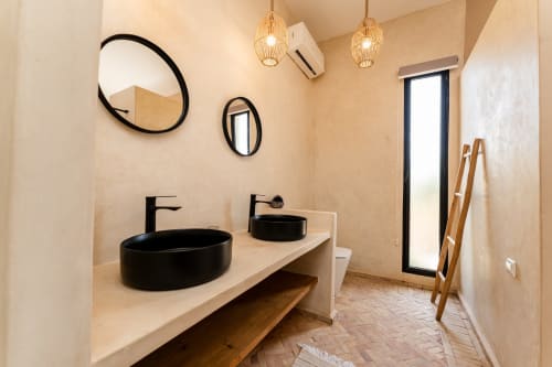Salle de bain moderne du Riad Arkaya à Essaouira avec deux vasques noires, miroirs et luminaires suspendus