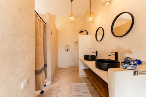 Salle de bains spacieuse dans la Chambre Mogador du Riad Arkaya à Essaouira, avec deux vasques noires, douche chauffée, luminaires suspendus