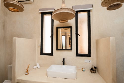 Salle de bain moderne du Riad Arkaya à Essaouira avec luminaires en suspension tressés, vasque design et miroirs à cadre noir