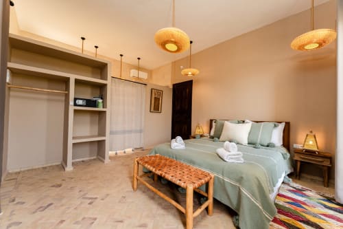 Chambre Enakhla au Riad Arkaya à Essaouira avec lit queen-size, luminaires suspendus tressés, vue sur le jardin et penderie ouverte
