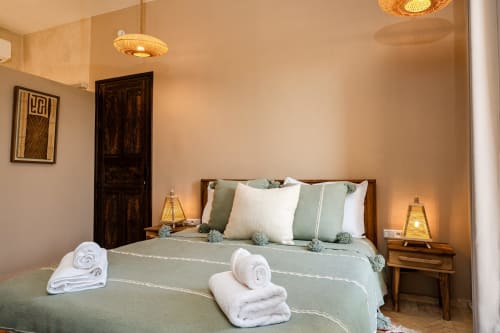 Chambre Enakhla au Riad Arkaya à Essaouira : lit queen-size aux draps verts, oreillers blancs, serviettes roulées, tables de nuit en bois