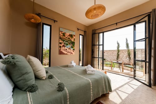 Chambre Riad Arkaya à Essaouira avec lit queen-size, luminaires suspendus tissés et terrasse avec vue sur le jardin et murs en pierre