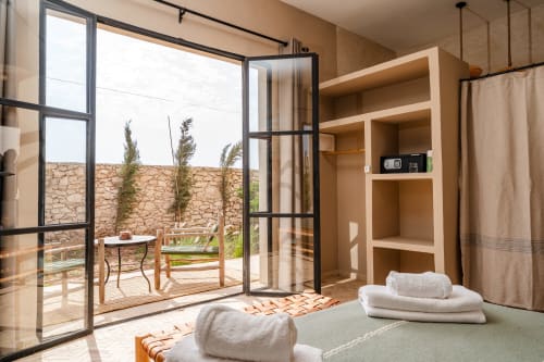Chambre lumineuse au Riad Arkaya à Essaouira avec terrasse vue jardin, étagères en bois, serviettes blanches et espace extérieur privé