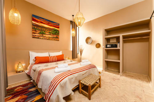 Chambre accueillante du Riad Arkaya à Essaouira aux murs orange chaud, lit queen-size, luminaires suspendus et rangements accessibles.