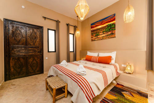 Chambre Argana au Riad Arkaya à Essaouira : spacieuse chambre accessible avec lit queen, porte sculptée traditionnelle, orange