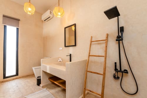 Salle de bains accessible du Riad Arkaya Essaouira avec équipements modernes, étagère en bois et douche à effet pluie noire