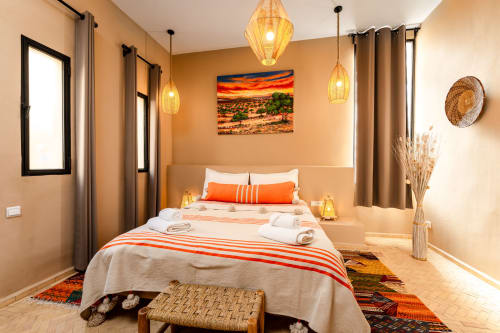 Chambre accessible au Riad Arkaya à Essaouira avec lit queen, accents orange, luminaires suspendus et vue sur la ville