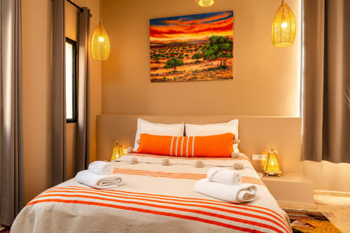 Chambre chaleureuse au Riad Arkaya à Essaouira avec accents orange, lit queen-size et tableau coucher de soleil africain
