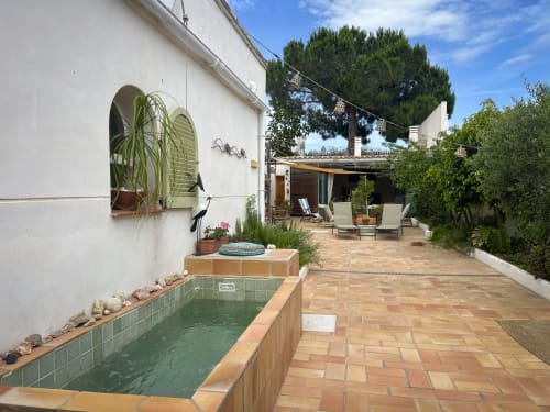 Terraza de Cala Pipa con piscina, edificio blanco, vegetación frondosa y zona de descanso en Poble Nou del Delta