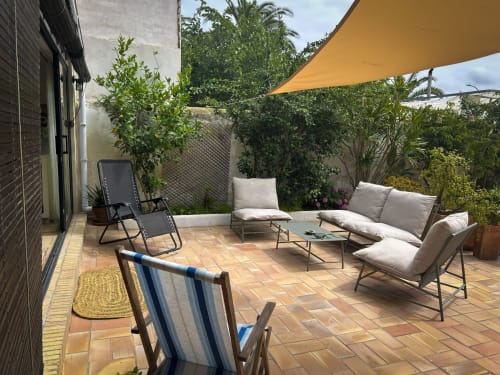 Terraza soleada del hotel Cala Pipa en Tarragona con asientos de descanso, vela de sombra amarilla y plantas verdes exuberantes