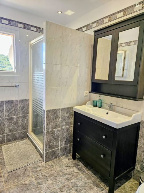 Modern bathroom in Villa Eva at Corsu Di Core, Favone, featuring black vanity, white sink, marble tiles, and glass shower