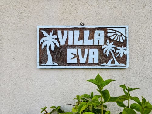 Villa Eva wooden sign with palm tree decorations on beige wall in Favone, Corsica