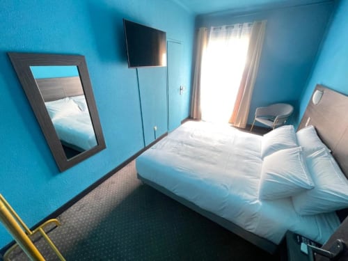 Chambre deluxe turquoise éclatante à l'Hôtel New Fregate à Canet-en-Roussillon avec lit blanc, TV et balcon portes vitrées