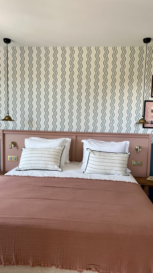 Chambre d'hôtel moderne au Saint Enogat de Dinard avec tête de lit rose, oreillers rayés et papier peint à motifs ondulés