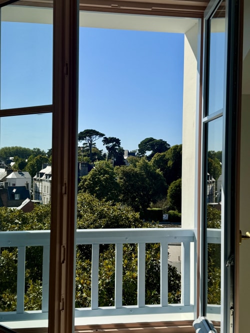 Portes-fenêtres ouvertes de l'Hôtel Saint Enogat à Dinard révélant une vue sur la ville, végétation luxuriante et bâtiments lointains