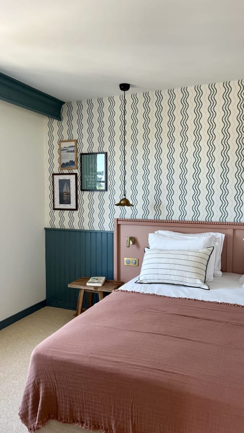 Lit jumeau dans une chambre de l'hôtel Saint Enogat avec papier peint ondulé, panneaux bleu-vert, tête de lit rose et fenêtre avec vue sur la ville