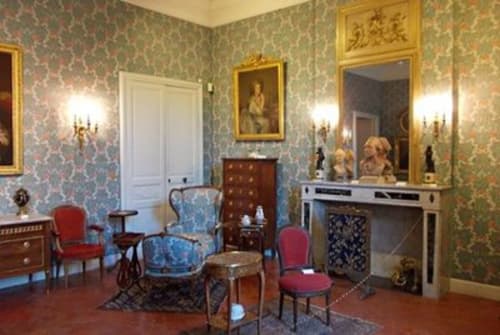 Élégante suite Oriflamme & Travertin avec papier peint damassé, cheminée, miroirs dorés, fauteuils en velours rouge et mobilier d'époque.