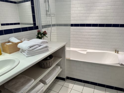 Salle de bains moderne à la Maison Melrose à Vouvray avec carrelage blanc, accents bleu marine, baignoire profonde et vanité organisée