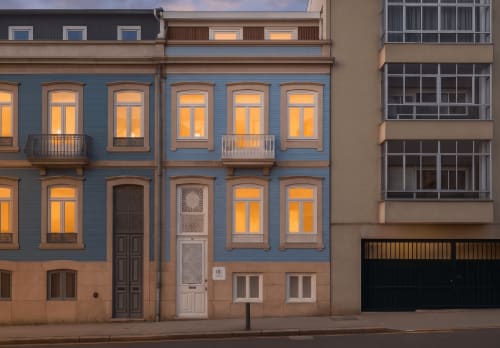 Fachada histórica azul e bege do Oporto Comfort Dom Hugo no Porto, Portugal, com janelas iluminadas ao anoitecer