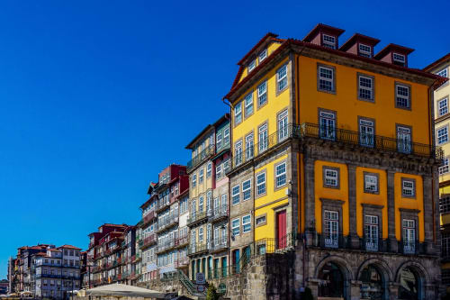 Edifícios históricos coloridos no Porto, Portugal com fachadas amarelas e vermelhas sob céu azul cristalino