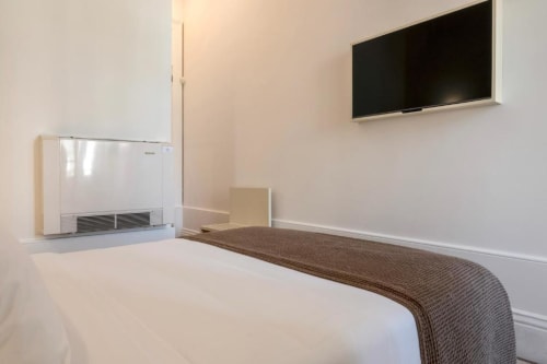 Quarto de hotel moderno com cama branca, TV de tela plana, aquecedor e decoração minimalista na Porto Charm House