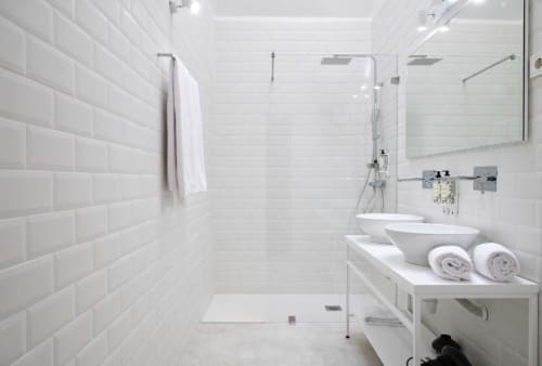 Banheiro moderno branco com azulejos tipo metrô, box de vidro, dois lavatórios suspensos, toalhas enroladas e artigos de higiene