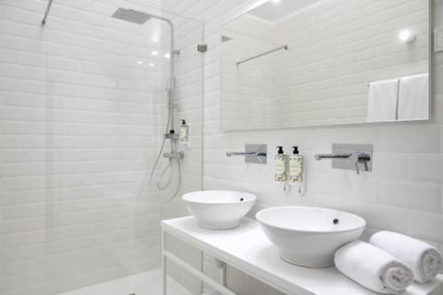 Banheiro moderno com dois lavatórios brancos suspensos, chuveiro tipo chuva e comodidades premium na Oporto Comfort Charming House Porto