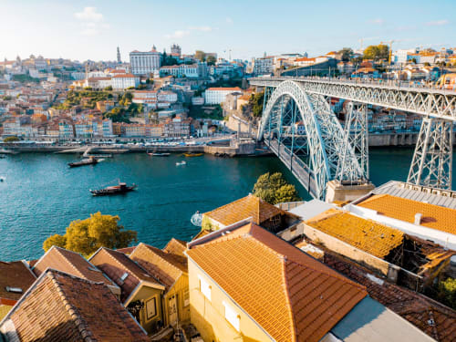 Vista aérea da frente ribeirinha colorida do Porto com Ponte Dom Luís, telhados de terracota e Rio Douro