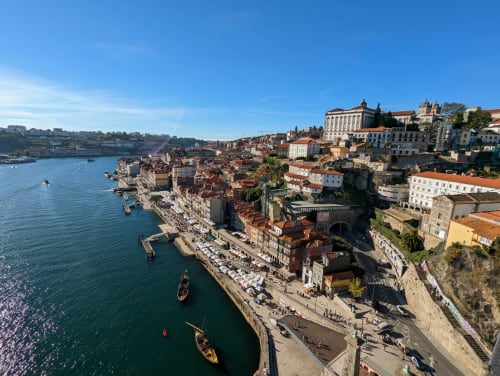 Vista aérea do histórico bairro ribeirinho do Porto com edifícios coloridos, rio Douro e barcos tradicionais ao longo da