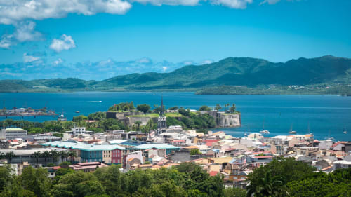 Auberge Sunshine Conciergerie à Fort-de-France surplombe une baie turquoise avec fort historique insulaire et montagnes verdoyantes