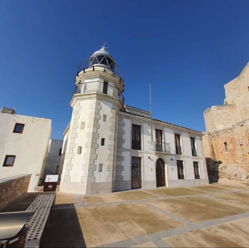 Historic lighthouse building in Peñíscola's old town plaza, white stone architecture under clear blue sky