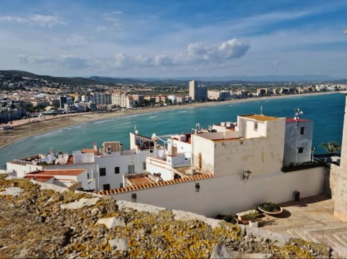 White Mediterranean apartment complex overlooking turquoise beach in Peñíscola, Spain with coastal city views