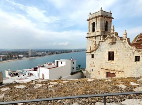 Historic church tower overlooking Peñíscola beach and Mediterranean Sea with white apartment building below