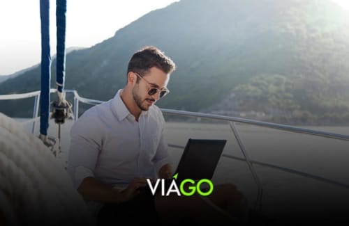 Man working on laptop aboard boat with mountain backdrop, RentalaYa! property manager software