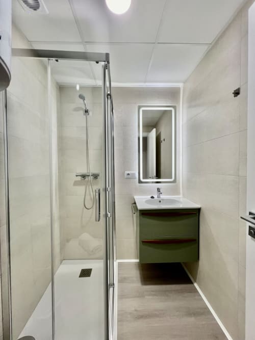 Baño moderno en Architettura Apartamentos Úbeda con ducha abierta, tocador verde y espejo iluminado