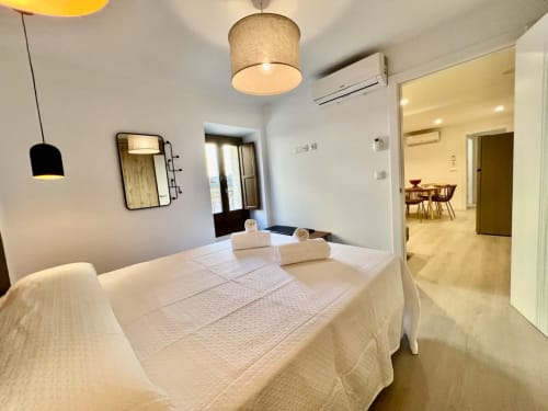Dormitorio moderno en Architettura Apartamentos de Úbeda, Jaén con cama blanca, iluminación colgante y sala de estar abierta