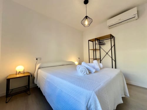 Dormitorio moderno en Architettura Apartamentos de Úbeda con ropa de cama blanca, lámpara colgante y vistas a la ciudad
