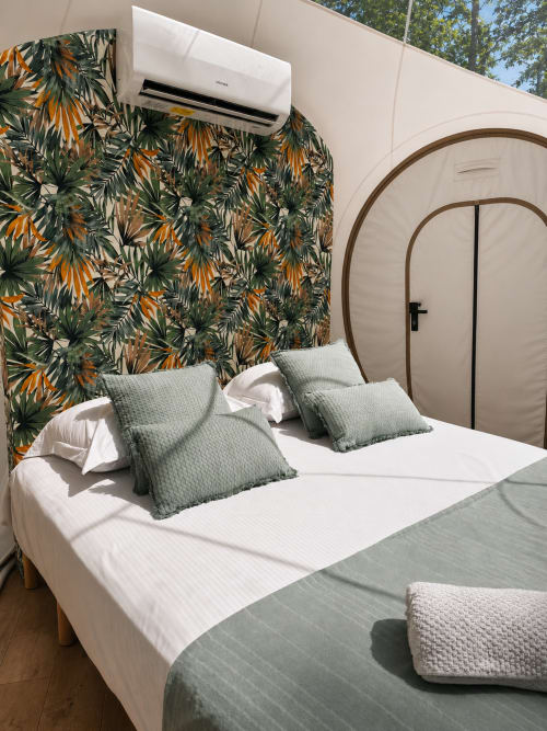 Chambre moderne à La Biche Au Bois avec tête de lit papier peint botanique, lit blanc, oreillers gris, tête de lit en bois voûté, et