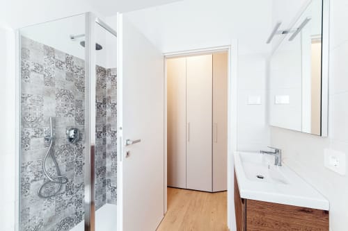 Bagno moderno a Lago Suites Como con doccia walk-in, lavabo bianco, specchio e pavimento in legno