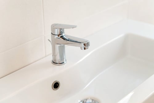 Rubinetto cromato moderno sopra lavabo bianco nel bagno di Lago Suites Como con parete piastrellata