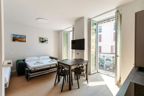 Camera moderna al Lago Suites Como con letto, TV a schermo piatto, tavolo da pranzo e balcone con vista sulla città