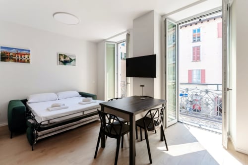 Camera moderna presso Lago Suites Como con letto, tavolo da pranzo, TV a schermo piatto e balcone con vista sulla città