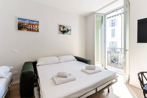 Camera moderna alle Lago Suites Como con letto matrimoniale, sedie verdi, balcone con vista sulla città e opere d'arte